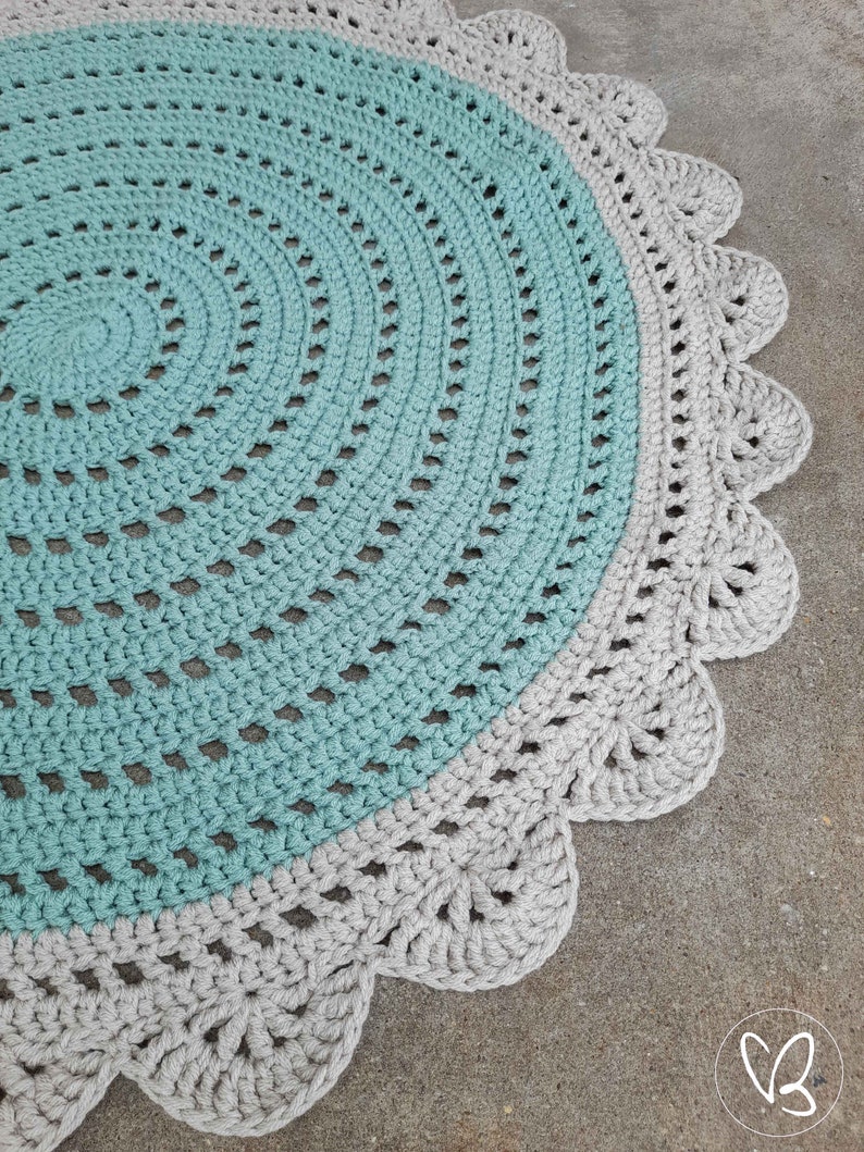 May include: A round crocheted rug with a light blue center and a gray outer border. The border has a scalloped edge.