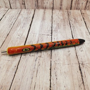 May include: A black and orange pen with a fish design. The pen is on a light wood background.