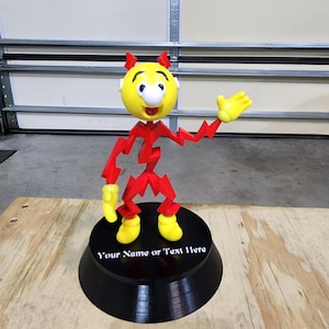 May include: A 3D-printed figurine of a cartoon character with a yellow head, red body, and yellow shoes and hands. The figurine is standing on a black base with the text "Your Name or Text Here".
