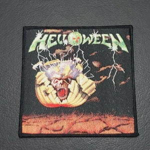 Puede incluir: Parche cuadrado con la palabra "HELLOWEEN" en verde, con un gráfico de monstruo. El monstruo tiene una boca roja y está rodeado de rayos sobre un fondo negro.