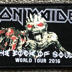 May include: Black and white Iron Maiden patch featuring a skeletal figure with red eyes and the text "The Book of Souls World Tour 2016".