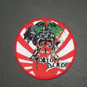 以下が含まれることがあります： 緑と黒のドラゴン、剣、そして「TOKYO BLADE」の文字が刺繍された赤、白、黒のワッペンです。