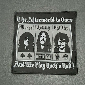 Può includere: Toppa ricamata in bianco e nero con il testo "The Afterworld Is Ours" e "And We Play Rock 'n' Roll!" La toppa presenta tre ritratti di musicisti con i nomi "Wurzel", "Lemmy" e "Philthy" sopra ogni ritratto. Il nome della band "Motörhead" è stampato sotto i ritratti.