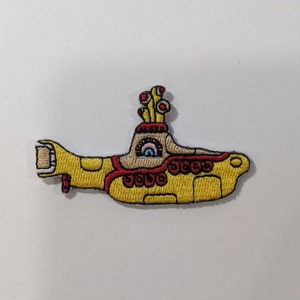 May include: Yellow submarine embroidered patch with red and white details. The submarine has a single eye with a rainbow iris and a periscope with a red and white striped top.