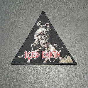 Könnte beinhalten: Schwarzer dreieckiger Patch mit einem weißen und roten gestickten Bild einer Kreatur, die eine Waffe hält, und dem Text "ICED EARTH".