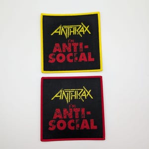 Puede incluir: Dos parches de tela negra con bordes amarillos y rojos. Los parches presentan el nombre de la banda "Anthrax" y el texto "I'm Anti-Social" en letras rojas y amarillas.