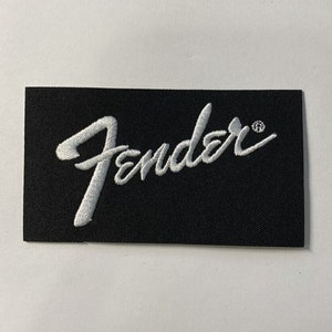 以下が含まれることがあります： 黒い布のパッチに白い刺繍で「Fender」のロゴが施されています