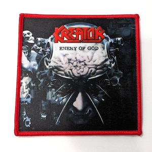 Puede incluir: Un parche bordado negro y rojo con el nombre de la banda "Kreator" y el título del álbum "Enemy of God". El parche presenta un gráfico de una cabeza robótica con un cerebro expuesto.