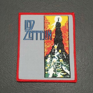 Puede incluir: Un parche bordado gris y rojo con las palabras "LED ZEPPELIN" en letras azules. El parche presenta una imagen colorida de una montaña con figuras escalando.