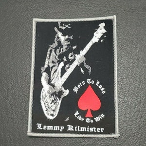 Puede incluir: Parche bordado en blanco y negro con una silueta de una persona tocando un bajo. El parche tiene un as de picas rojo con el texto "Born To Lose Live To Win" y "Lemmy Kilmister" en la parte inferior.
