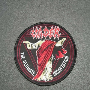 May include: A black and red circular patch with the band name "VADER" in red lettering. The patch features a stylized image of a person in a red robe with the text "THE ULTIMATE INCANTATION" around the edge.