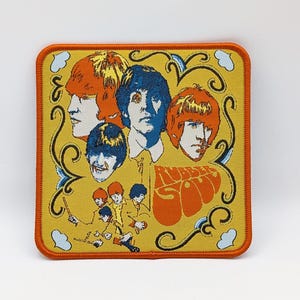 Może przedstawiać: Naszywka haftowana na żółto i pomarańczowo przedstawiająca zespół czterech mężczyzn z napisem "Rubber Soul" w kolorze pomarańczowym i żółtym.