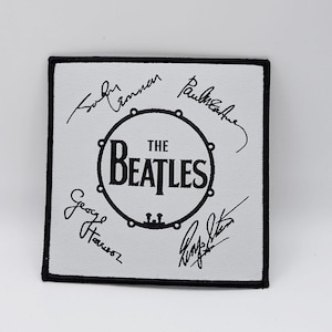 May include: A white fabric patch with black embroidery of a drum with the text "THE BEATLES" inside. The signatures of John Lennon, Paul McCartney, George Harrison, and Ringo Starr are embroidered around the drum.