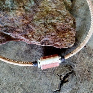 May include: A tan leather cord necklace with a cylindrical pendant. The pendant is made of red, white, and silver materials.