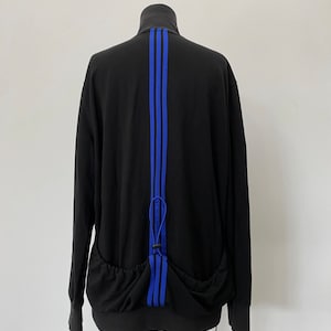 May include: Black zippered jacket with blue stripes down the back. The jacket has a drawstring at the bottom.
