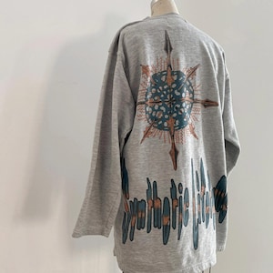May include: Gray long-sleeve sweatshirt with a graphic print of a blue and orange compass with the text "Synthetic Lifeforms" in blue and orange.