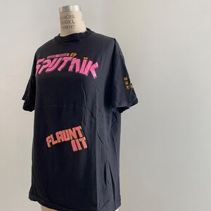 May include: Black t-shirt with pink and yellow text that reads "Show Single 12" and "FLaunt It" with the word "SPUTNIK" in a stylized font.