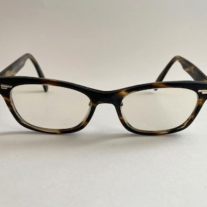 May include: A pair of tortoiseshell eyeglasses with clear lenses. The glasses have a classic, rectangular shape with a slight cat-eye flair.