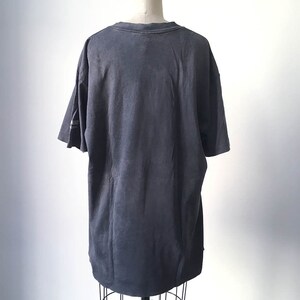 Puede incluir: Una camiseta gris carb&oacute;n de gran tama&ntilde;o, exhibida en un maniqu&iacute;. La camiseta tiene mangas cortas y cuello redondo. La tela parece suave y ligeramente descolorida. El dise&ntilde;o es simple y casual.