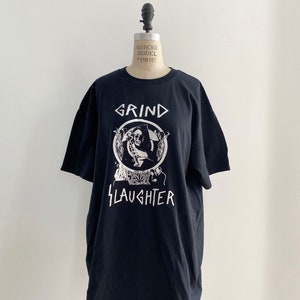 May include: Black t-shirt with a white graphic of a skull in a circle with the words "Grind Slaughter" below it.