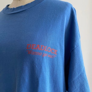 May include: A blue t-shirt with a red graphic that says "DEADLOCK" and "Wanna get wet?"