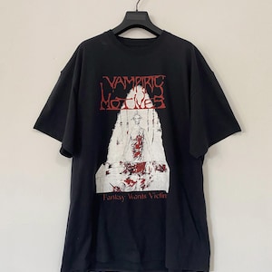 May include: Black t-shirt with a white graphic print of a person in a red dress with the text "Vampiric Motives" and "Fantasy Wants Victim" in red.