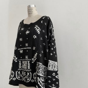 May include: Black and white patterned sweater with a paisley design. The sweater has a loose fit and long sleeves.