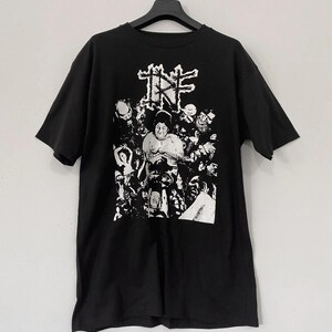 May include: Black t-shirt with a white graphic print of a band called "Infest". The graphic features a large, central image of a person surrounded by smaller images of people and faces.