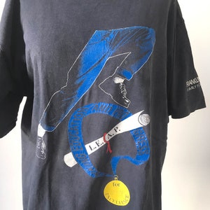 Puede incluir: Camiseta gris oscuro con un gr&aacute;fico azul y blanco de piernas en movimiento, un diploma y una medalla de oro. El texto en la camiseta incluye "L.E.A.P." y "for EXCELLENCE". La camiseta tambi&eacute;n tiene el texto "FRANKLIN FAMILY FOUNDATION".