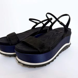 May include: A pair of black platform sandals with a navy blue satin base and a white and black sole. The sandals have a black strap across the toes and an ankle strap. The platform measures approximately 2 inches.