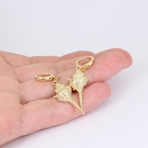 May include: A pair of gold-coloured seashell earrings. Each earring features a detailed, textured seashell pendant hanging from a small hoop. The earrings are designed to be worn on the ear.