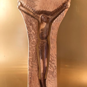 May include: A wooden sculpture of a person on a cross. The sculpture is carved from a single piece of wood and has a rustic, natural look.