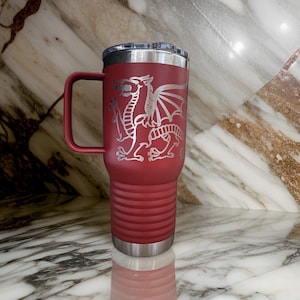 May include: A red stainless steel travel mug with a silver lid and handle. The mug has a laser-etched design of a silver dragon on the front.