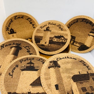 May include: Set of six cork coasters featuring different lighthouses with their names engraved on each coaster. The lighthouses are depicted in black and white, and the coasters are brown.
