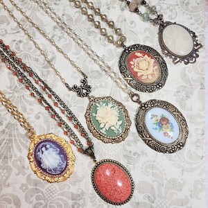 May include: A collection of vintage-style necklaces with ornate pendants. The pendants feature cameo designs, floral motifs, and a coral-colored stone. The chains vary in style and color, including gold, silver, and beaded strands.
