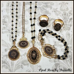 May include: Gold-toned jewelry set featuring necklaces, rings, and a bracelet. The necklaces have black beaded chains and ornate pendants with a starburst design. The rings and bracelet also feature the starburst design. The jewelry is displayed on a patterned background.