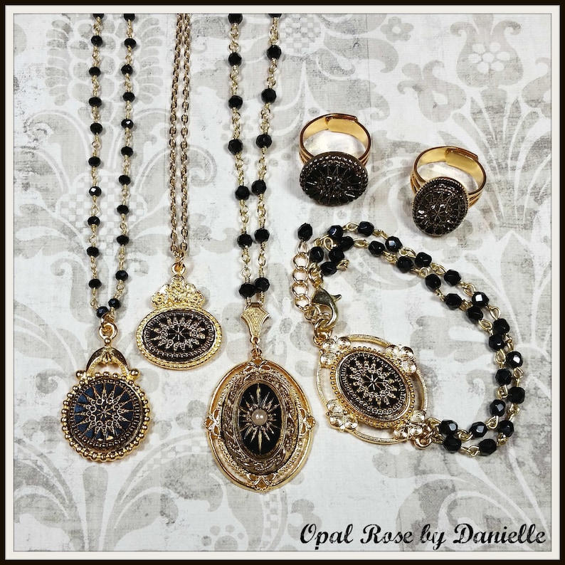 May include: Gold-toned jewelry set featuring necklaces, rings, and a bracelet. The necklaces have black beaded chains and ornate pendants with a starburst design. The rings and bracelet also feature the starburst design. The jewelry is displayed on a patterned background.