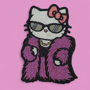 May include: Embroidered patch featuring a stylized cat wearing sunglasses, a purple fur coat, and a gold chain. The cat has a pink bow and is set against a pink background. The patch has a glittery texture.