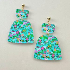 May include: Two-piece, turquoise earrings with a gold-colored post. The earrings feature a floral and alligator pattern in pink, green, and yellow. The top piece is rectangular, and the bottom piece is a rounded shape.
