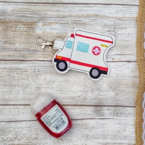 May include: White ambulance keychain with a red cross and a small red hand sanitizer bottle.