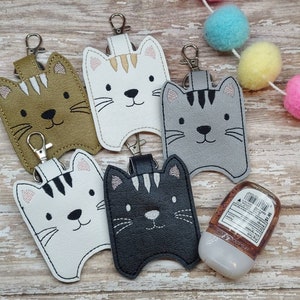 Puede incluir: Cinco portadesinfectantes para manos con forma de gato con llaveros. Los portadesinfectantes están hechos de piel sintética y están disponibles en marrón, blanco, gris, negro y blanco con rayas negras. Los portadesinfectantes están todos unidos a llaveros y son perfectos para llevar desinfectante de manos para llevar.
