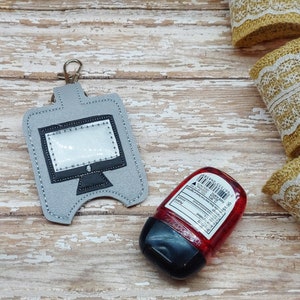 May include: A gray fabric keychain with a clear plastic window shaped like a computer monitor. The keychain has a silver metal ring and a black strap. A small red plastic bottle of hand sanitizer is also in the image.