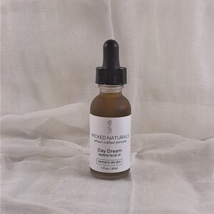 Puede incluir: Una botella de vidrio de aceite facial etiquetada "WICKED NATURALS artisan crafted skincare Day Dream daytime facial oil normal to dry skin 1 fl oz/30ml"