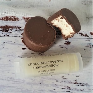 Puede incluir: Un tubo de bálsamo labial natural de malvavisco cubierto de chocolate Wicked Naturals. El tubo es transparente y muestra el bálsamo en el interior. El producto es de 0,15 oz / 4 gramos. Se muestran dos malvaviscos cubiertos de chocolate en el fondo.