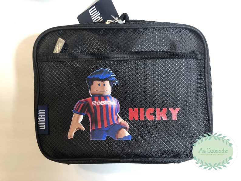 May include: Black lunch bag with a mesh design, featuring a Roblox character in a red and blue striped jersey. The name "NICKY" is printed in red. Includes a Wildkin tag.