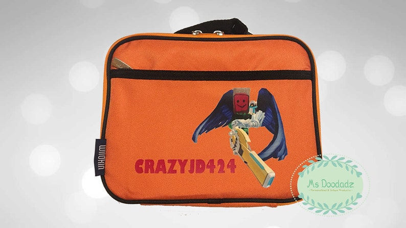 May include: Orange lunch bag with a black zipper and handle. The bag features a graphic of a character with blue wings and a weapon, along with the text "CRAZYJD424". A small tag reads "WIIKIN".