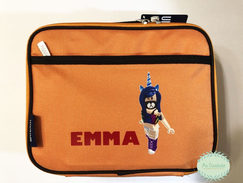 May include: Orange rectangular lunch bag with a black zipper and trim. The bag features the name "EMMA" in red block letters and a cartoon unicorn character. A small pocket is on the front.