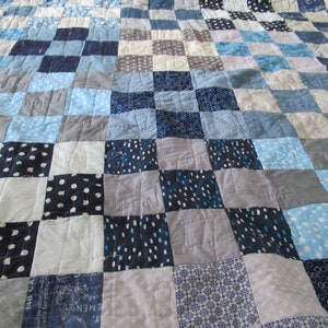 May include: A patchwork quilt in shades of blue, grey, and white. The squares feature patterns like polka dots and stars. The quilt is made of soft fabric. The quilt's design is reminiscent of a checkerboard.