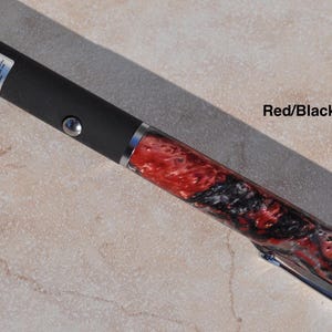 May include: A laser pointer featuring a matte black cylindrical body with a silver button and a warning label near the tip. The lower section displays a marbled red and black resin pattern with a silver pocket clip and a polished silver end cap.