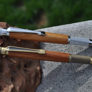 以下が含まれることがあります： 金属製のアクセントが付いた木製のペンが2本。上のペンは銀色のクリップと先端、下のペンは金色のクリップと先端です。